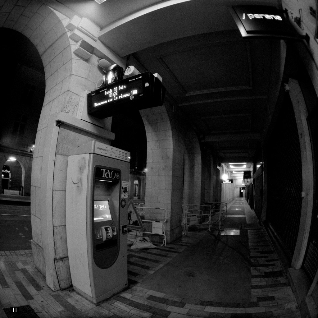 Une vue en noir et blanc d'un passage souterrain la nuit, avec un distributeur automatique et des panneaux d'affichage au-dessus.