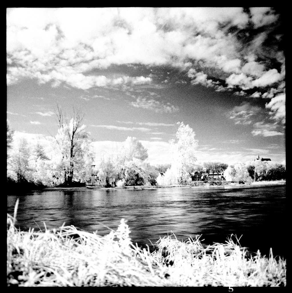 Infrared photography of a river. Leaves and clouds are white and the sky is dark.